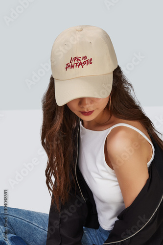 Cropped upward shot of a dark-haired girl, wearing beige baseball cap with print with lettering 