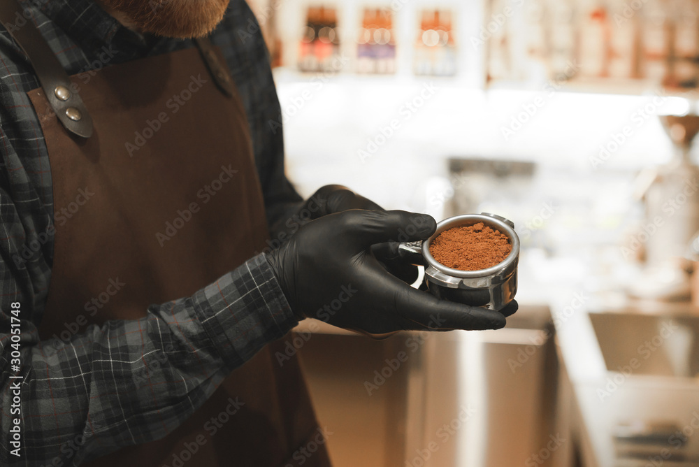 Male coffee shop owner holding a portafilter with coffee and preparing latte and cappuccino. Barista with coffee holder at the cafe making coffee. Close up photo, hands only, unrecognizable.