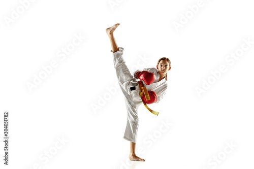 Confident junior in kimono practicing hand-to-hand combat, martial arts. Young female fighter with yellow belt s training on white studio background. Concept of healthy lifestyle, sport, action.