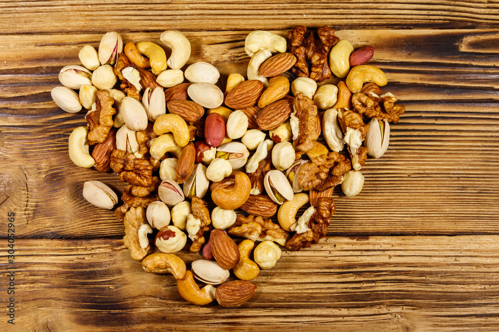 Pile of mixed nuts in shape of heart on wooden table. Top view. Walnuts, pistachio, almond, peanut, cashew, hazelnut on wood background. Healthy eating concept Pile of mixed nuts in shape of heart on wooden table. Top view. Walnuts, pistachio, almond, peanut, cashew, hazelnut on wood background. Healthy eating concept