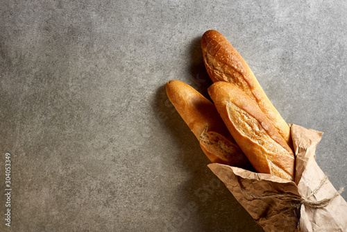 Fresh french baguettes packed in paper on a gray stone surface. Top view. photo