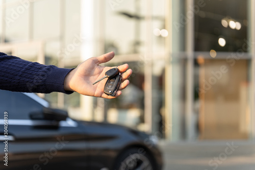 Hand with keys from a luxury black car on the background of the dealership. Dealership of rent, hire cars. Carsharing © Aleksandr