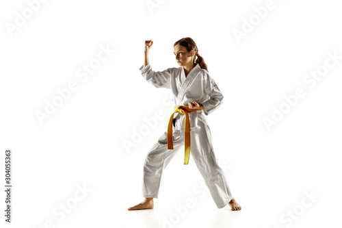 Confident junior in kimono practicing hand-to-hand combat, martial arts. Young female fighter with yellow belt s training on white studio background. Concept of healthy lifestyle, sport, action.