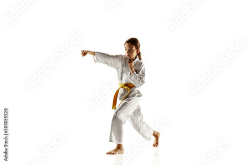 Confident junior in kimono practicing hand-to-hand combat, martial arts. Young female fighter with yellow belt s training on white studio background. Concept of healthy lifestyle, sport, action. © master1305