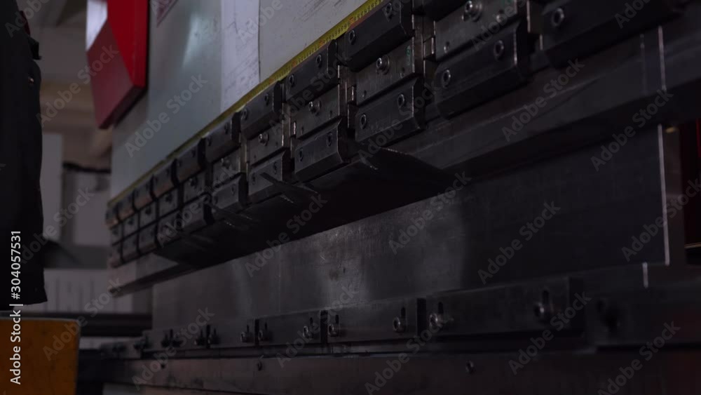 Automated process of manufacturing metal workpieces of certain shape, worker uses machine in factory floor, metal part bends in half under high pressure, smooth and accurate bending, work in factory Automated process of manufacturing metal workpieces of certain shape, worker uses machine in factory floor, metal part bends in half under high pressure, smooth and accurate bending, work in factory