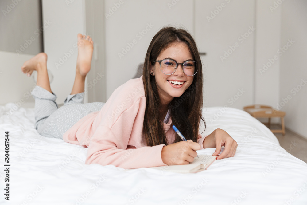 Cheerful lovely young girl wearing pajamas laying in bed Cheerful lovely young girl wearing pajamas laying in bed