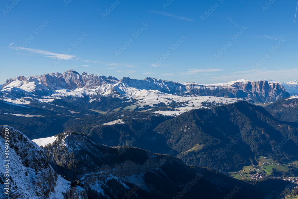 Seceda in the Italian Dolomites under snow. The background is a blue sky with clouds