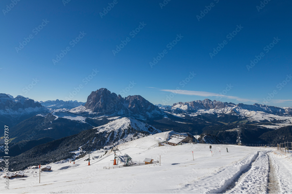 Seceda in the Italian Dolomites under snow. The background is a blue sky with clouds