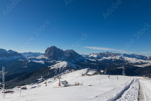 Seceda in the Italian Dolomites under snow. The background is a blue sky with clouds