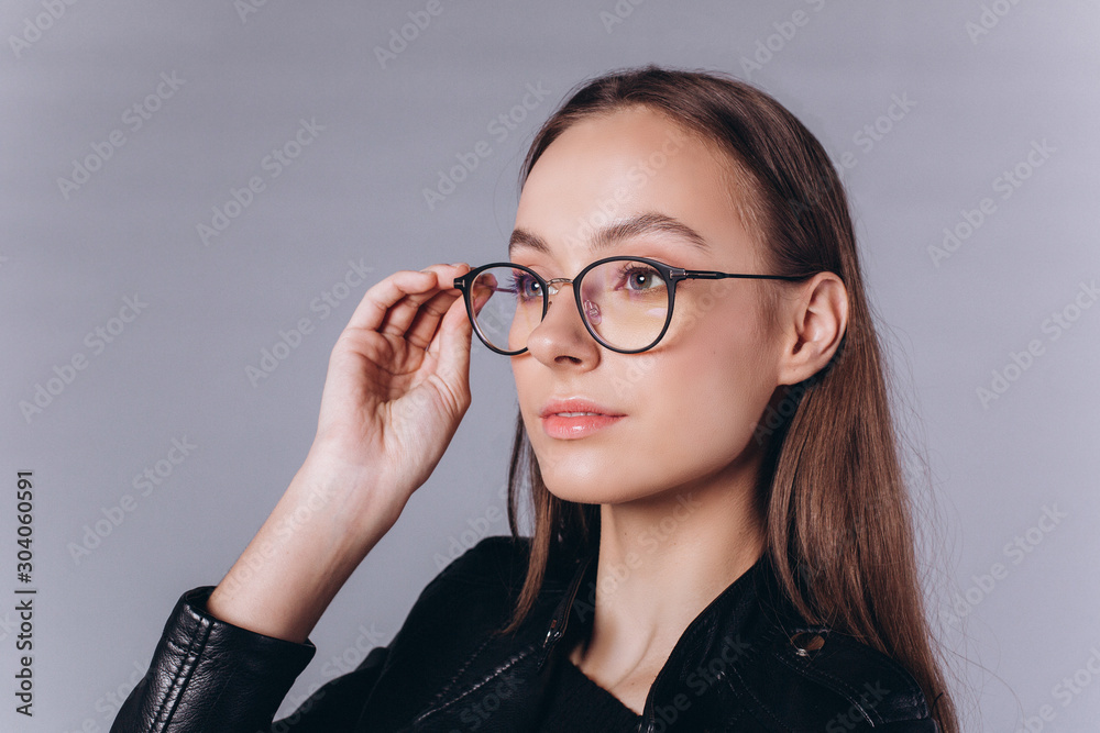 Studio close up portrait of young beautiful caucasian model in glasses posing on grey isolated background