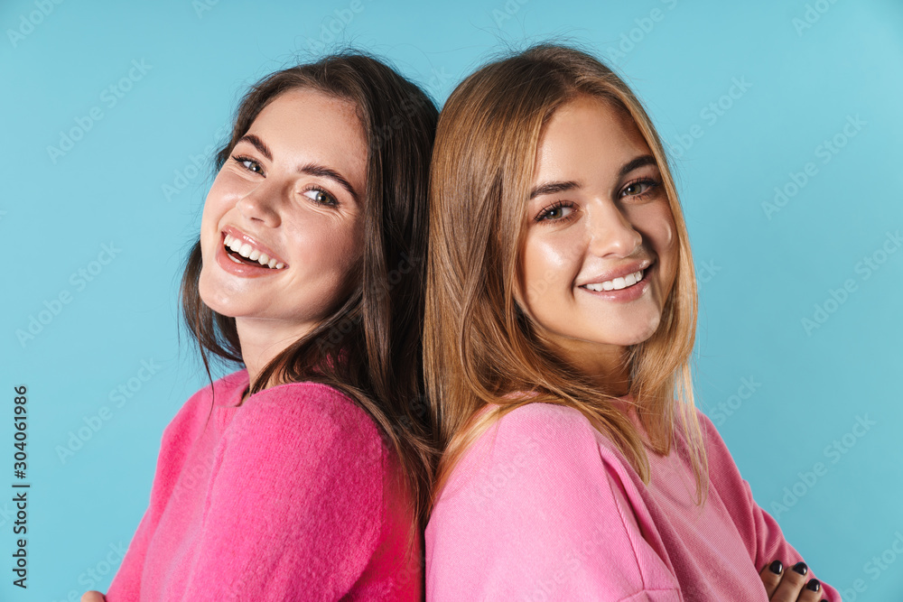 Photo of joyful young women standing back to back and smiling Photo of joyful young women standing back to back and smiling