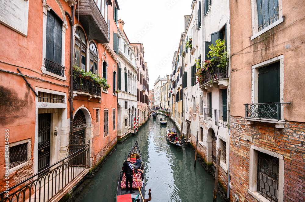09.10.2019 Venice, Italy, gondola with tourists floating on a narrow channel with turquoise water. The historic center of the city, Windows with wooden shutters.