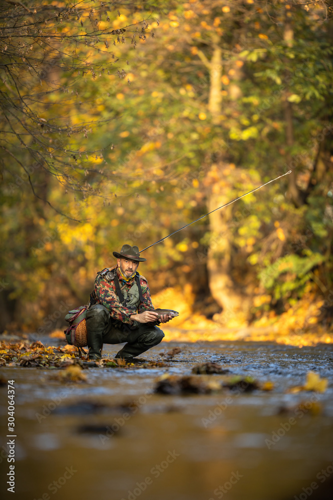 Handsome fly fisherman working the line and the fishing rod while fly fishing on a splendid mountain river for rainbow trout