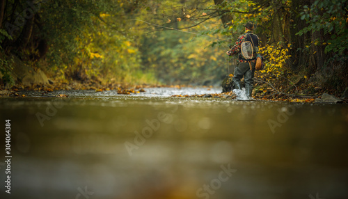 Handsome fly fisherman working the line and the fishing rod while fly fishing on a splendid mountain river for rainbow trout photo