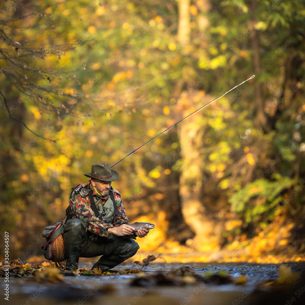 Handsome fly fisherman working the line and the fishing rod while fly fishing on a splendid mountain river for rainbow trout Handsome fly fisherman working the line and the fishing rod while fly fishing on a splendid mountain river for rainbow trout