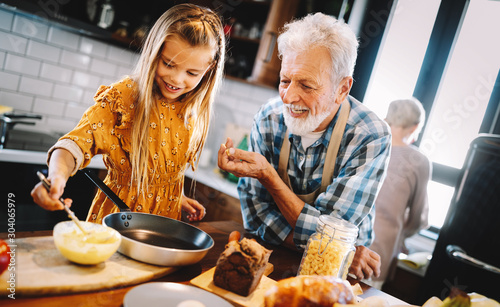 Happy young girl and her grandfather cooking together in kitchen photo