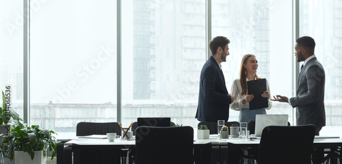 Businesspeople talking in office, standing against window photo