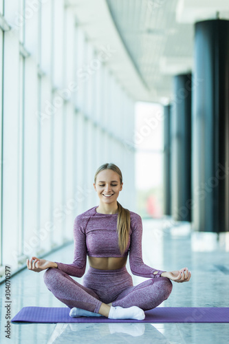 Fototapeta Naklejka Na Ścianę i Meble -  Yoga in studio. Keep calm. Attractive young woman sitting on lotus position on floor with eyes closed.