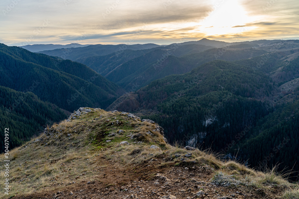 Naklejka premium Beautiful sunset in Rhodope mountains during the autumn with green trees in the hills and clouds in the sky