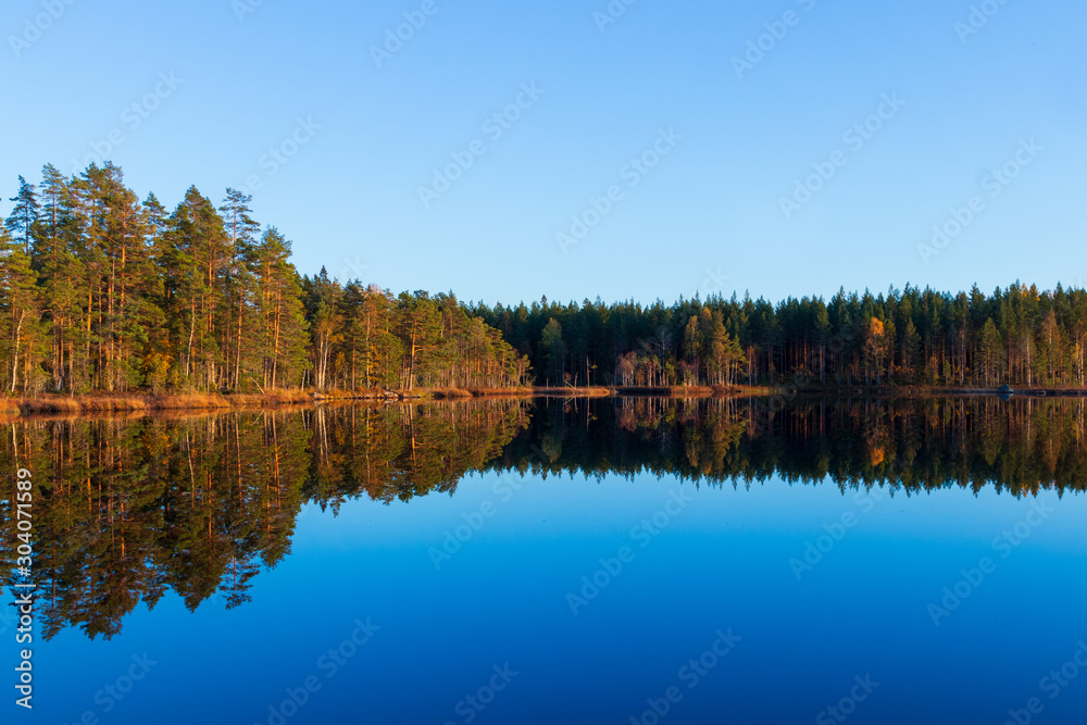 Sunset over a calm lake creating a mirror reflection inside a forest during autumn. Sunset over a calm lake creating a mirror reflection inside a forest during autumn.