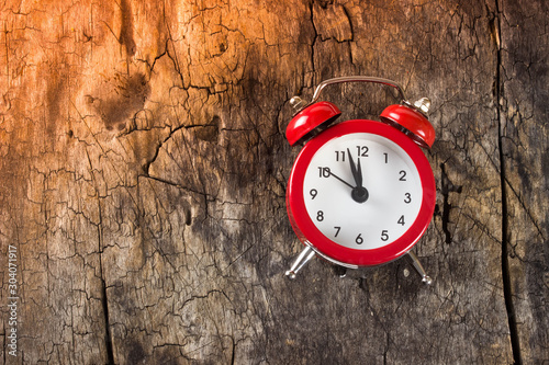 Red alarm clock on wooden background. On the clock is 11 hours and 55 minutes. Concept of time, Christmas and New year.