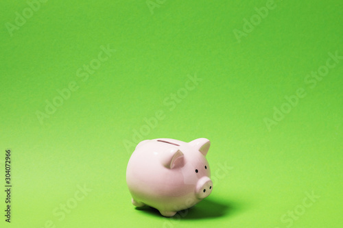 Pink piggy bank on green paper background with copy space