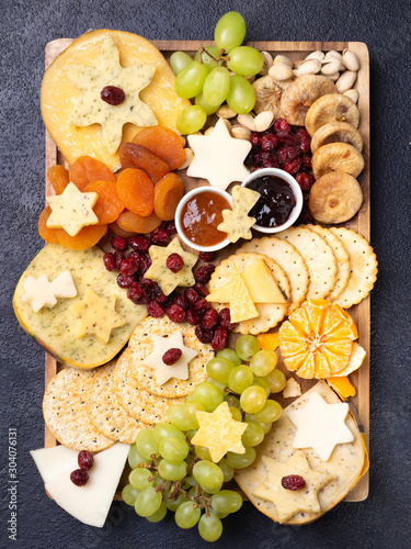 Cheese board appetizers platter with various types of cheese plate, grapes, dried figs, cranberries, pistachios and jams on dark background. Overhead view, cope space.