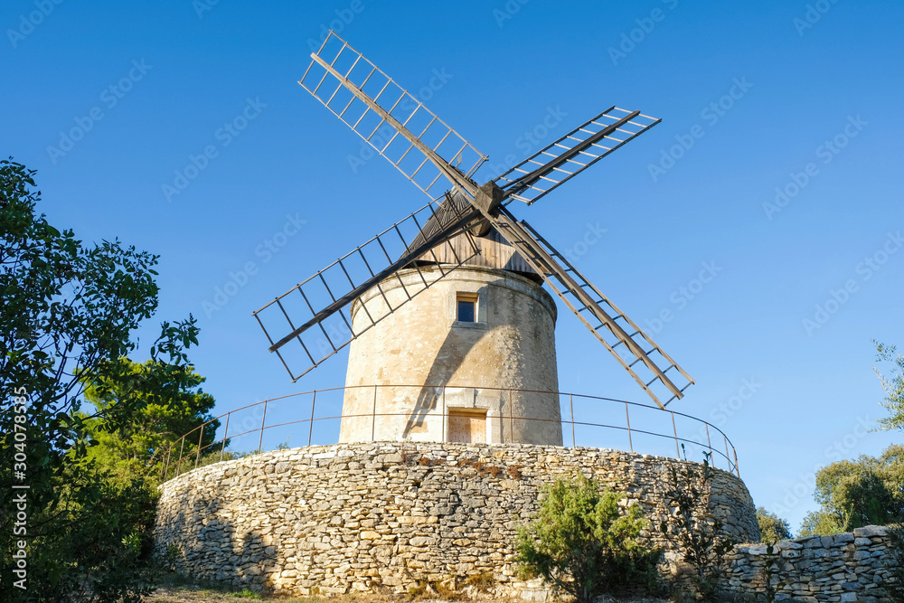 Joucas. Provence. France. October 05.2019. Editorial. Old windmill on a stone stand in the park under the evening sun.