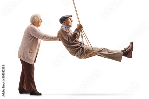 Senior woman pushing swinging a senior man on a wooden swing photo