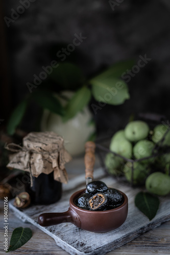 Jar of walnut jam on a wooden table and a group of green walnuts.