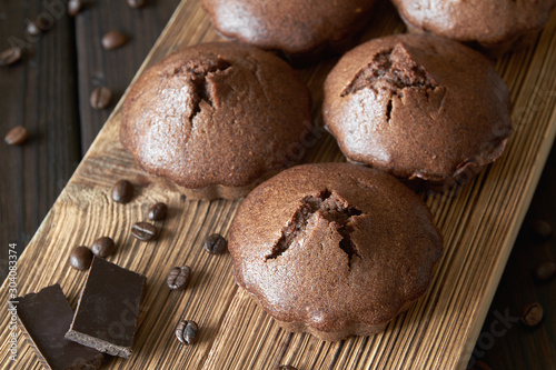 A group of homemade chocolate muffins on a wooden board with coffee beans and pieces of chocolate. Dark wooden background, closeup, selective focus