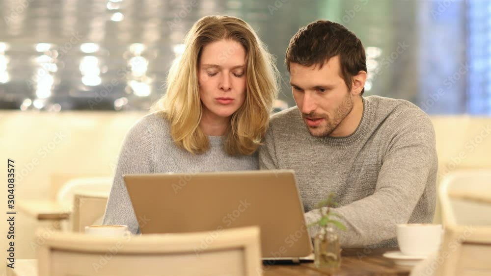 Front view of excited couple cheking laptop content sitting in a coffee shop in the Front view of excited couple cheking laptop content sitting in a coffee shop in the
