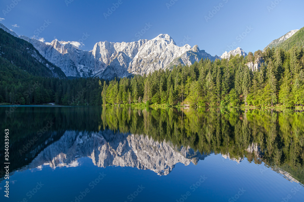 Scenic panoramic view of idyllic alpine mountain lake with crystal clear reflections in beautiful morning light at sunrise on a sunny day with blue sky in springtime