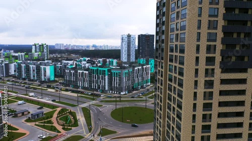 Flying of drone above apartment blocks in suburb. Modern residential area with playground, cars parked along street. Sleeping area in ecologically clean area near forest away noisy city.