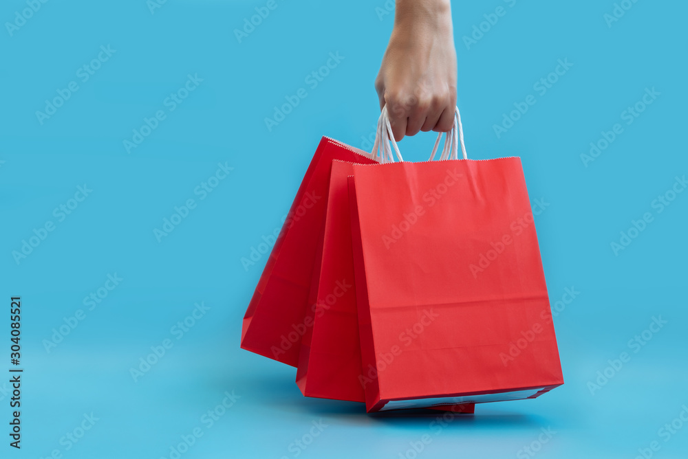 Hand holding red papers bag on blue background. Christmas and New Year holidays or sale concept. Copy space. Mock-up