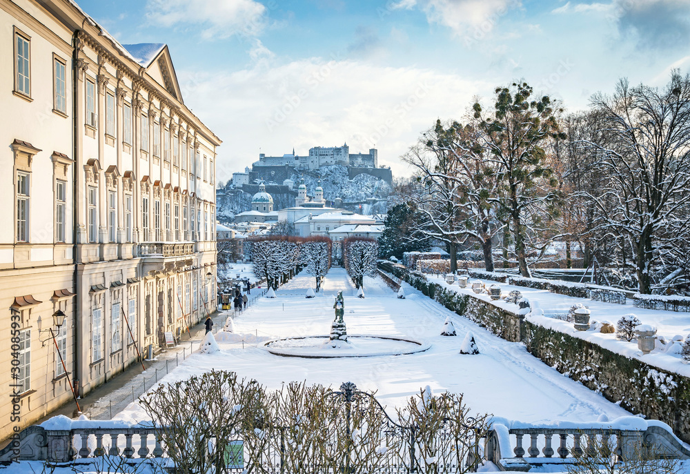 Fototapeta premium Klasyczny widok na słynne Ogrody Mirabell w historycznym mieście Salzburg z Twierdzą Hohensalzburg w złotym wieczornym świetle w piękny słoneczny dzień z błękitnym niebem zimą, Salzburger Land, Austria