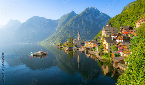 Classic panoramic view of famous old town Hallstatt and alpine deep blue lake with tourist ship in scenic golden morning light on a beautiful sunny day at sunrise in summer, Salzkammergut, Austria photo
