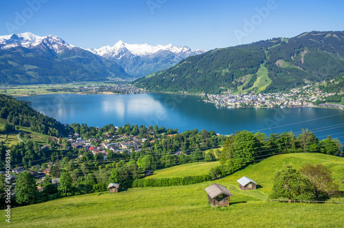 Panoramic view of beautiful scenery in the Alps with clear lake, green meadow, blooming flowers, traditional alpine chalets on a sunny day with blue sky in spring, Zell am See, Salzburger Land, Austri photo