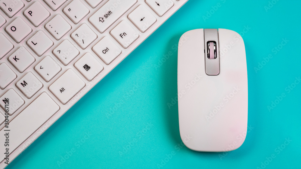 A wireless mouse lies next to a white computer keyboard. Blue background. Close-up. The concept of the office manager or computer salon selling peripheral devices. A wireless mouse lies next to a white computer keyboard. Blue background. Close-up. The concept of the office manager or computer salon selling peripheral devices.