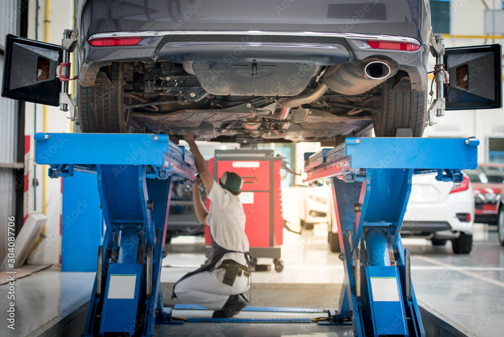 Fototapeta premium Car mechanic installing sensor during suspension adjustment. Wheel alignment work at repair service station