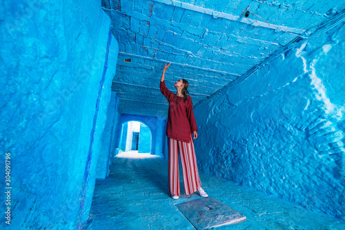 tourist in asian clothes stands in the tunnel of the blue city of morocco and touches the ceiling with his hand © nelen.ru