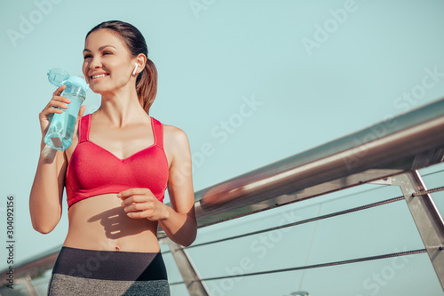 attractive brunetter after exercising drinking water on the bridge photo