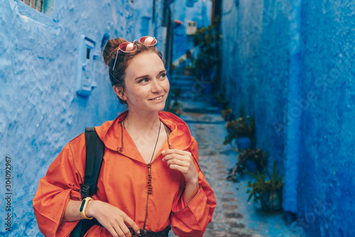 tourist in bright orange clothes with a backpack and sunglasses cute diminishes in the blue city of morocco © nelen.ru