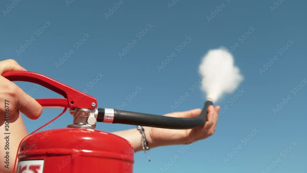 SLOW MOTION, CLOSE UP, DOF: Unrecognizable person squeeze the handle of a fire extinguisher, causing white smoke and foam to come out of the nozzle. Young woman uses a fire extinguisher outdoors.
