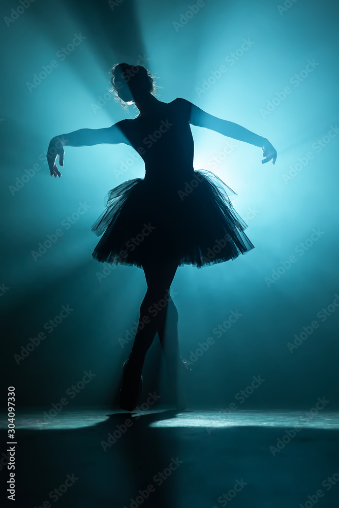 Fototapeta Młoda piękna balerina na scenie dymu taniec nowoczesny balet. Wykonuje płynne ruchy dłońmi na tle reflektorów. Kobieta w czarnej tutu kostium na scenie.