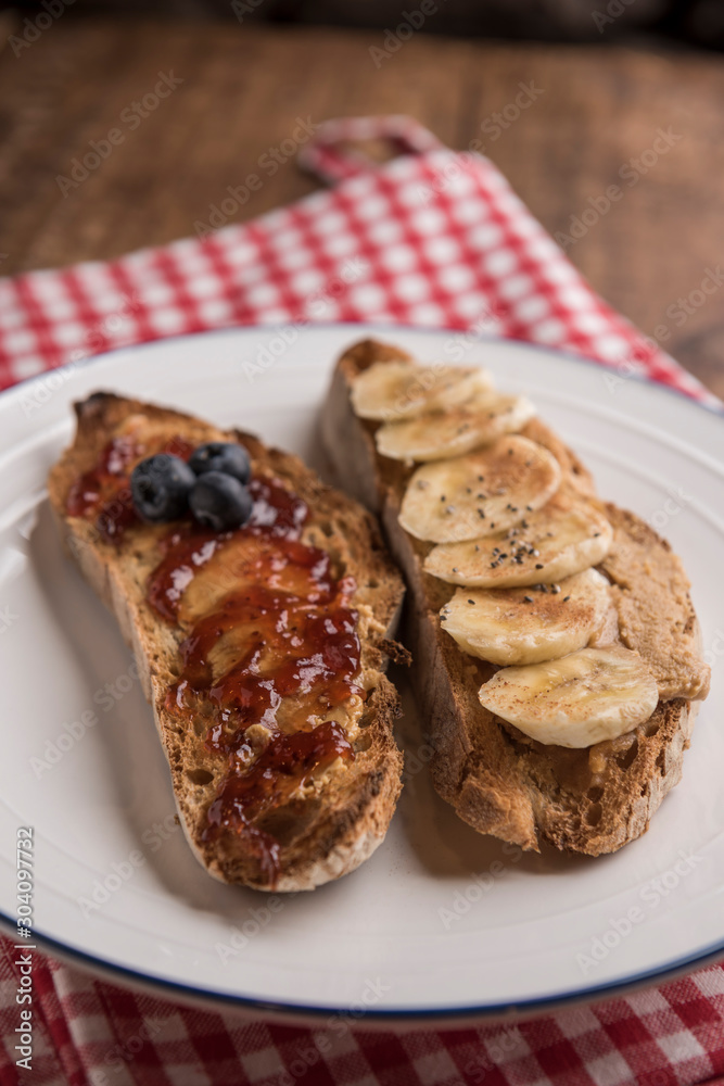 Slices of rustic bread with peanut butter, banana, blueberries, cinnamon, maple syrup and strawberry jam. Vertical, copyspace. Slices of rustic bread with peanut butter, banana, blueberries, cinnamon, maple syrup and strawberry jam. Vertical, copyspace.
