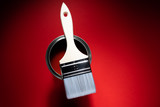 White brush on a can with red paint on a red background