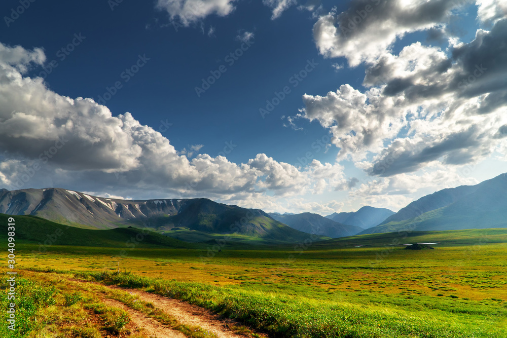 Fototapeta premium Panoramic landscape of the mountain range. Green mountain pass on a sunny day with clouds.