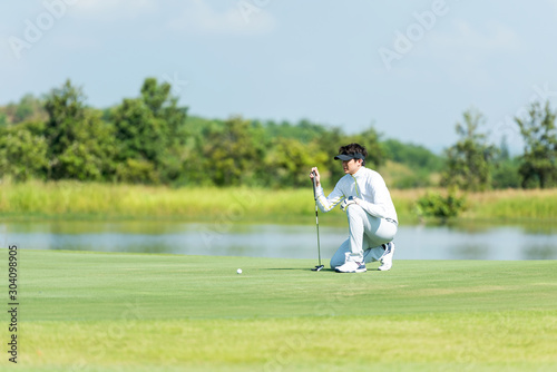 Professional Golfer asian man playing aiming shot for putting ball on the hole with club on green course. Hobby in holiday and vacations in sunny morning day on club golf. Lifestyle and Sport Concept
