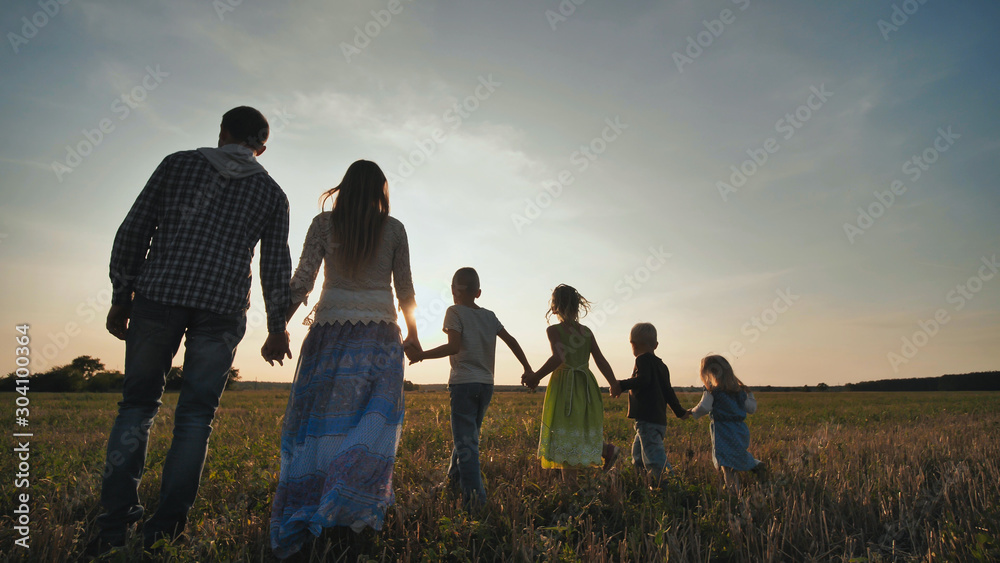 A large family of six people walk on the floor at sunset. - obrazy, fototapety, plakaty 
